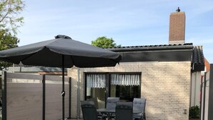 Eine Terrasse mit Tisch und Stühlen, ein überdachter Sitzbereich und eine Backsteinmauer.