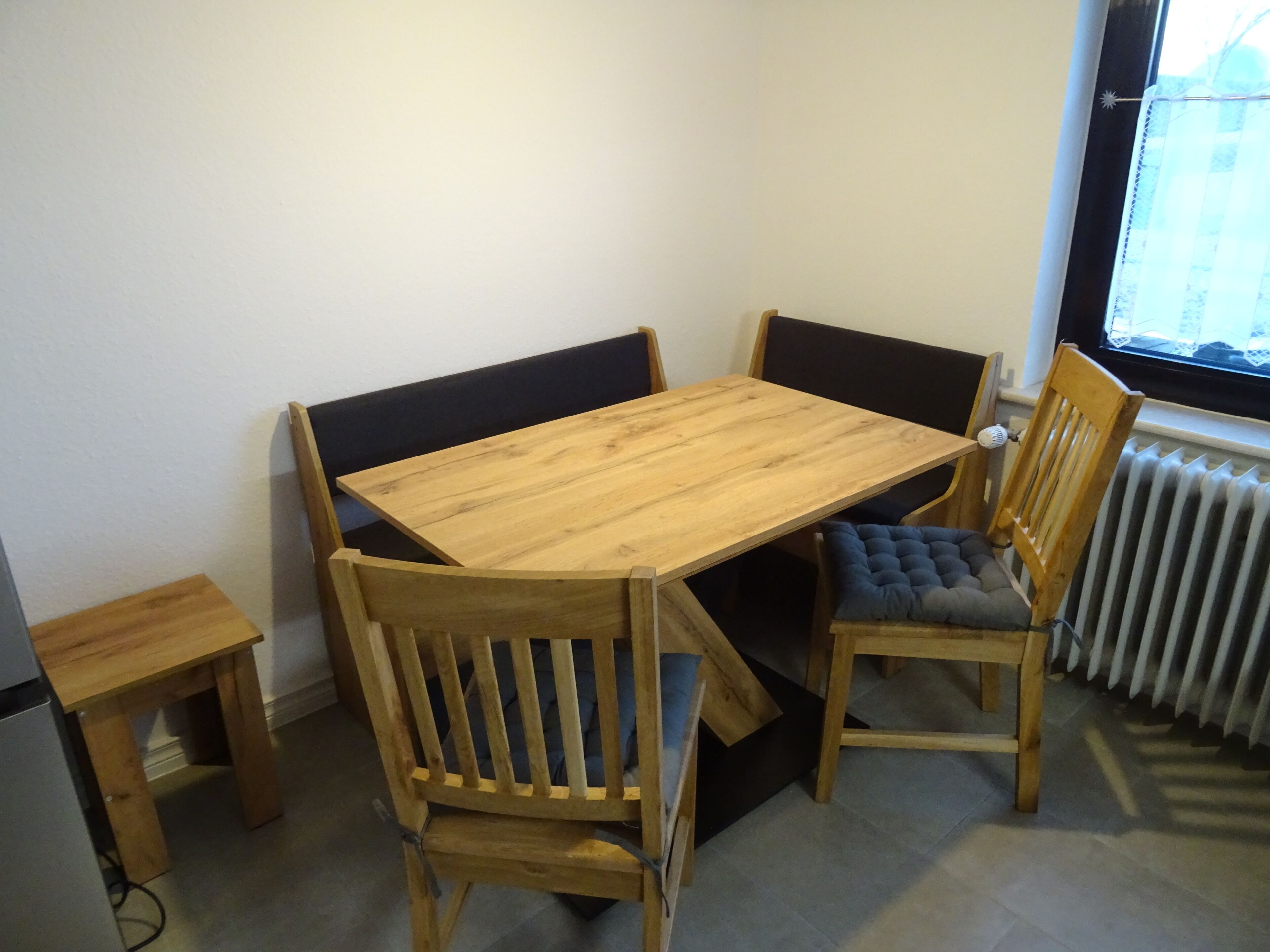 A wooden dining table with four chairs, a small side table, and a radiator near a window.