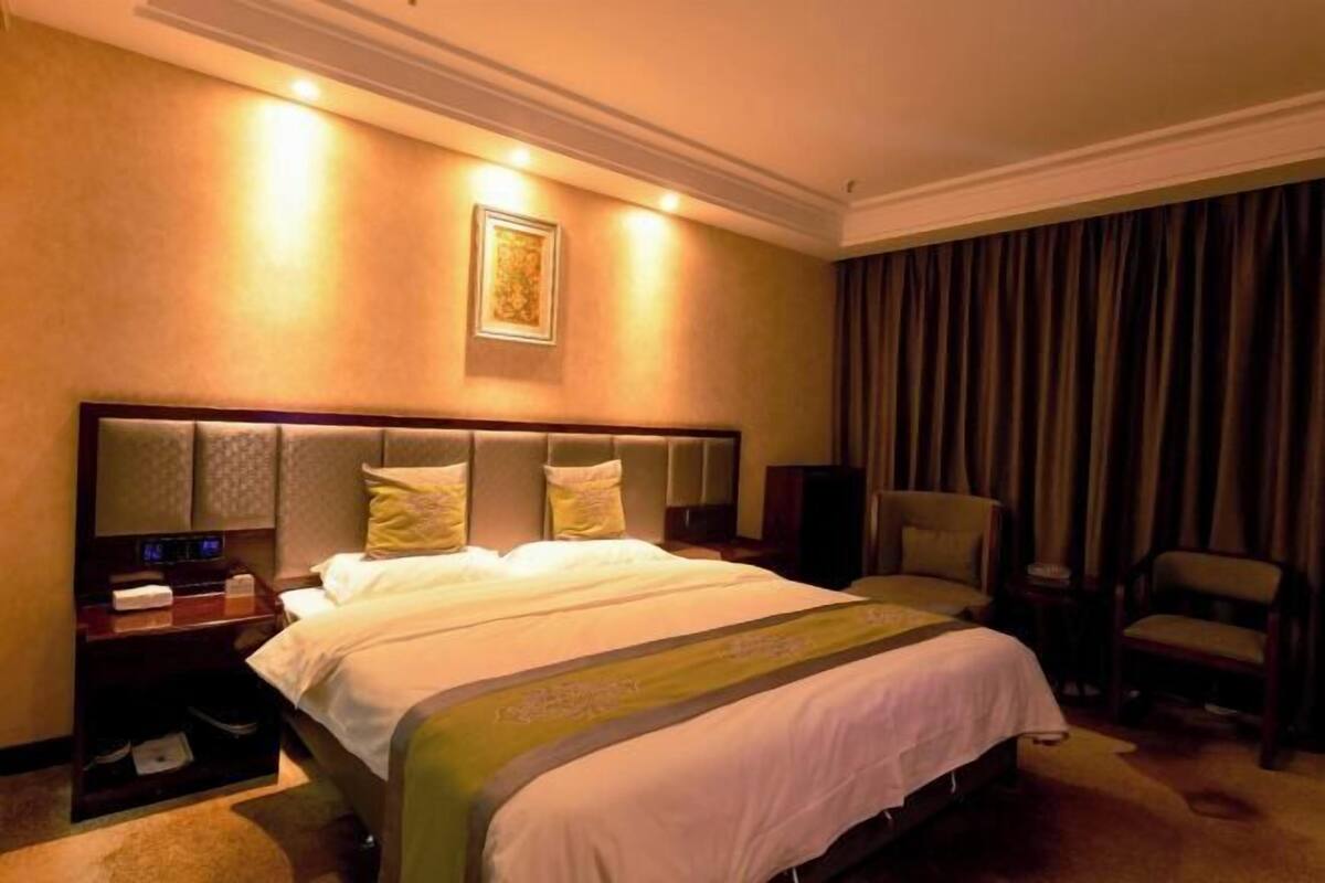 Ein Hotelzimmer mit einem großen Bett, einem Nachttisch, einem Sessel und einem an der Wand befestigten Fernseher.