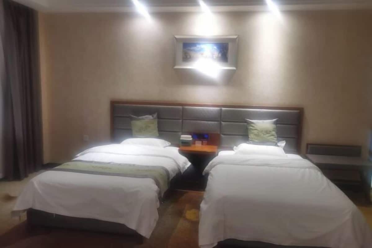 Ein Hotelzimmer mit zwei Betten, einem Nachttisch, einem gerahmten Bild an der Wand und einem Fenster mit Vorhängen.