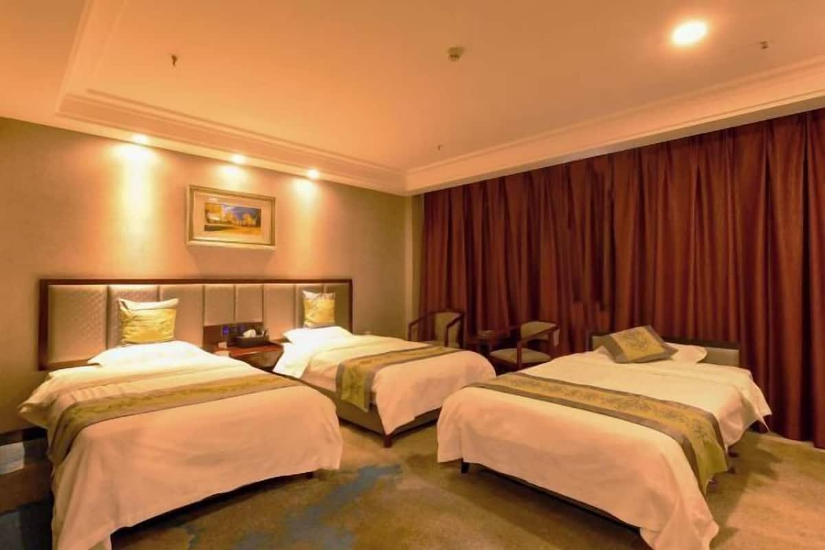 Ein Hotelzimmer mit zwei Betten, einem Kopfteil, einem Nachttisch, einem Sessel und einem großen Fenster mit Vorhängen.