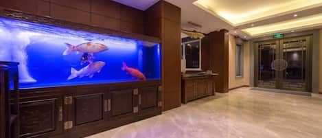A hotel lobby with a large aquarium, marble flooring, and a reception area with a glass door.