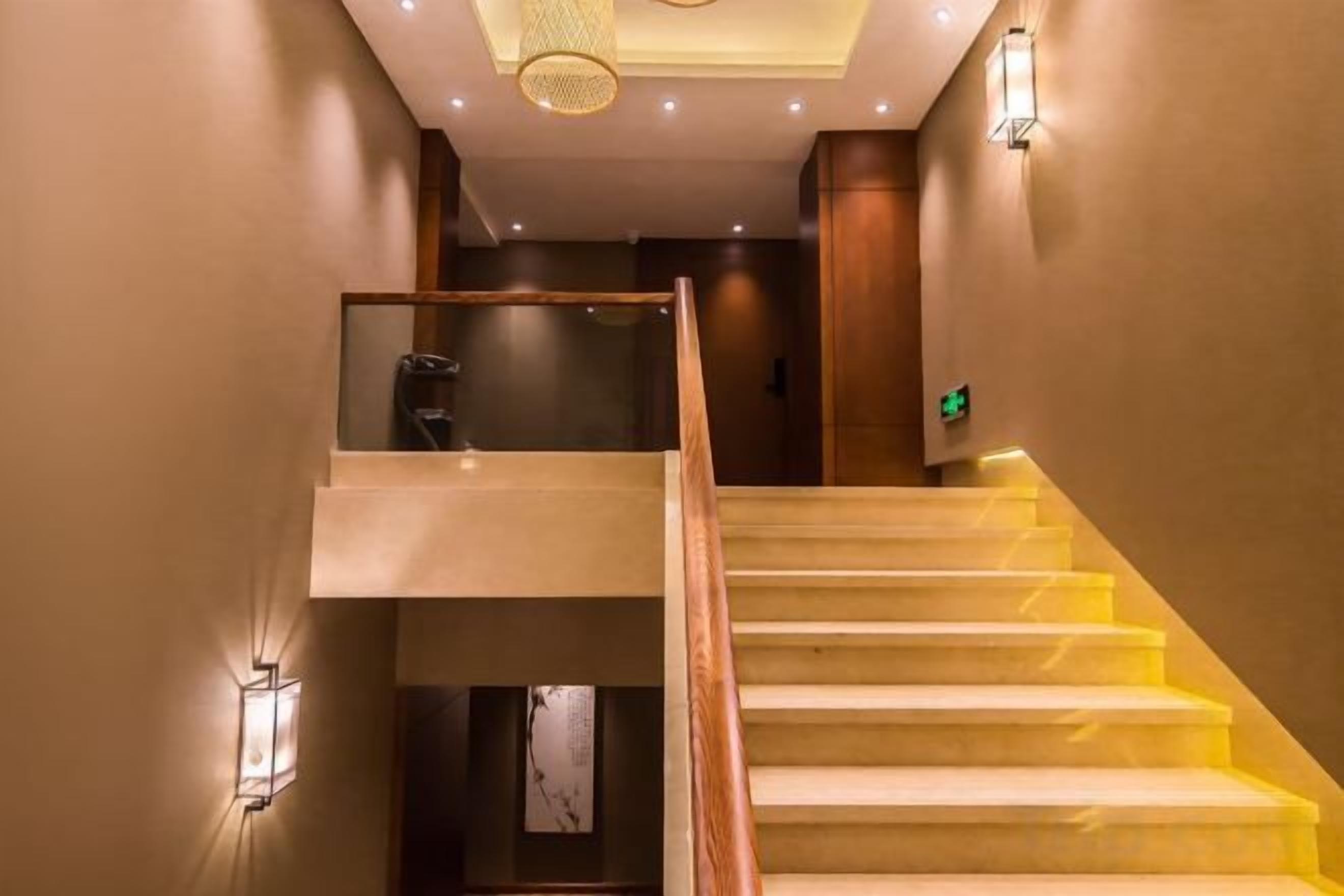 A staircase with a glass balustrade, a wooden handrail, and wall-mounted lighting fixtures.