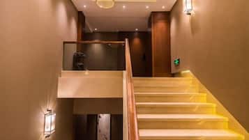 A staircase with a glass balustrade, a wooden handrail, and wall-mounted lighting fixtures.