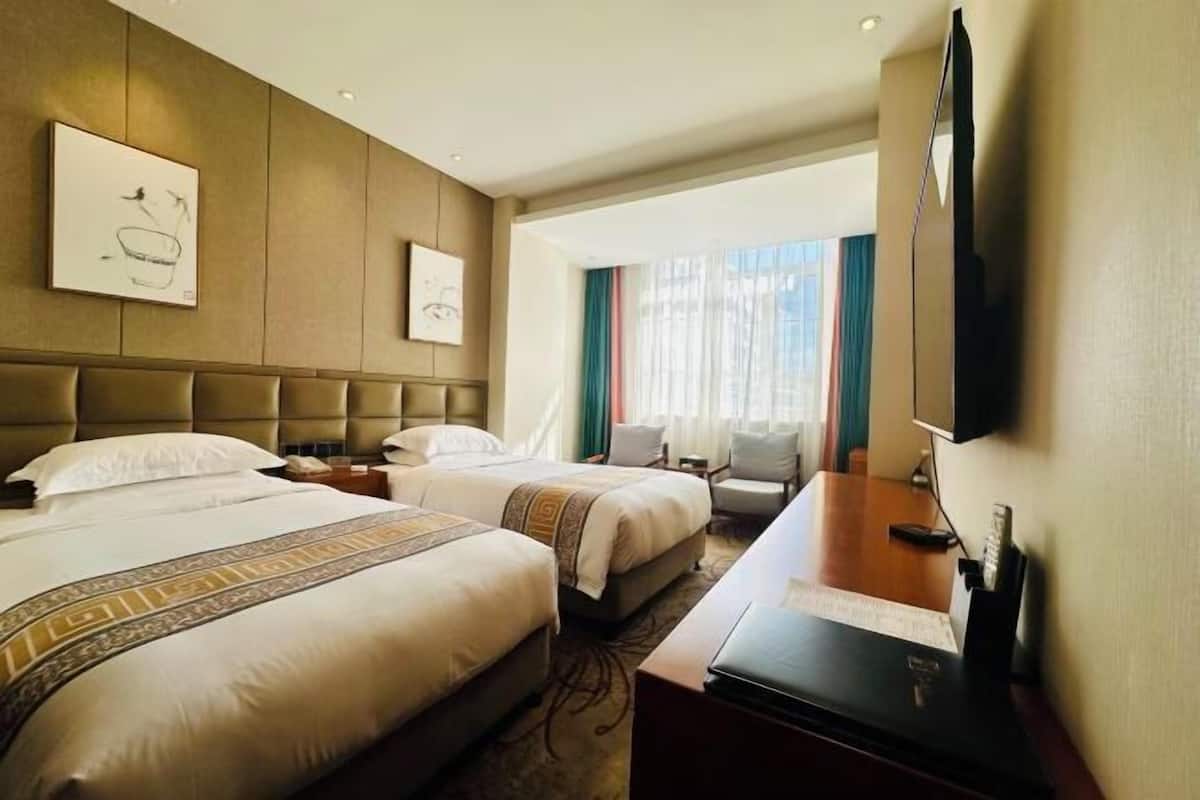Habitación de hotel con dos camas, un escritorio, un televisor y obras de arte en las paredes.