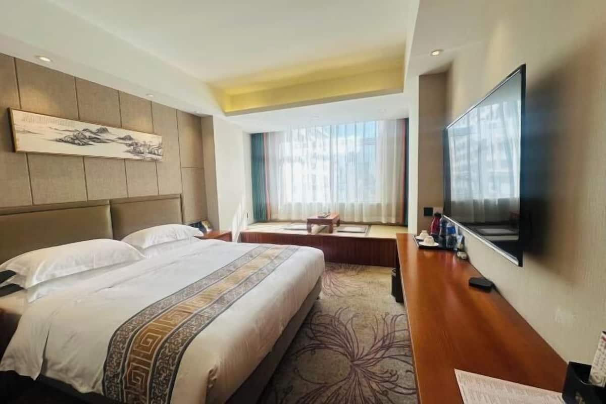 Habitación de hotel con una cama grande, un televisor de pantalla plana, un escritorio y una ventana con cortinas.