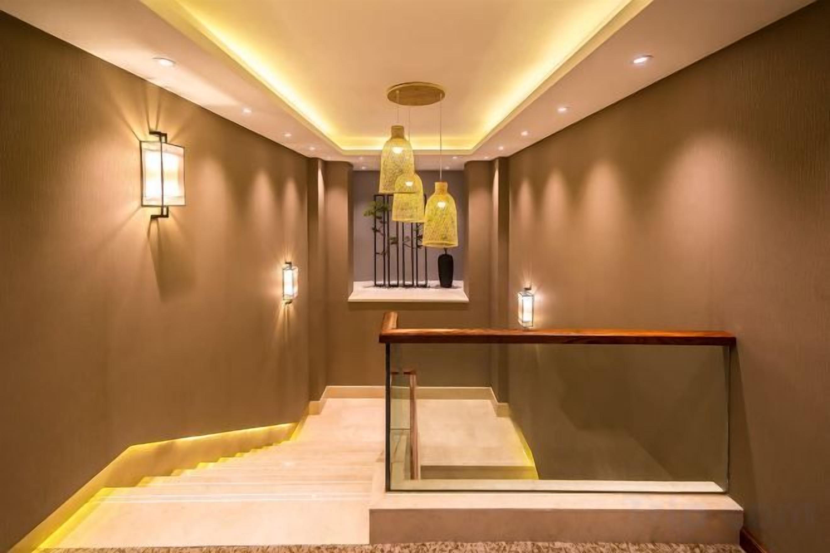 Una escalera moderna con barandas de vidrio y un pasamanos de madera, que conduce a un rellano con una lámpara.