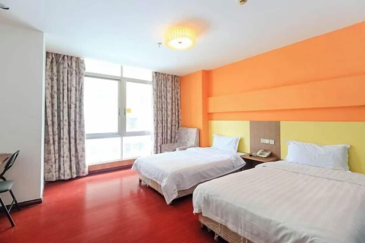 Habitación de hotel con dos camas, un escritorio, una silla y un ventanal con cortinas.