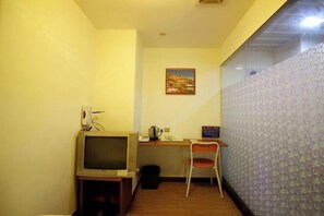 A small room with a wooden desk, a chair, a television, and a patterned wall.