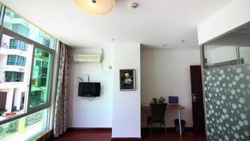 Una habitación con un ventanal grande, un televisor de pantalla plana montado en la pared, un escritorio con una silla y una puerta que da a otra habitación.