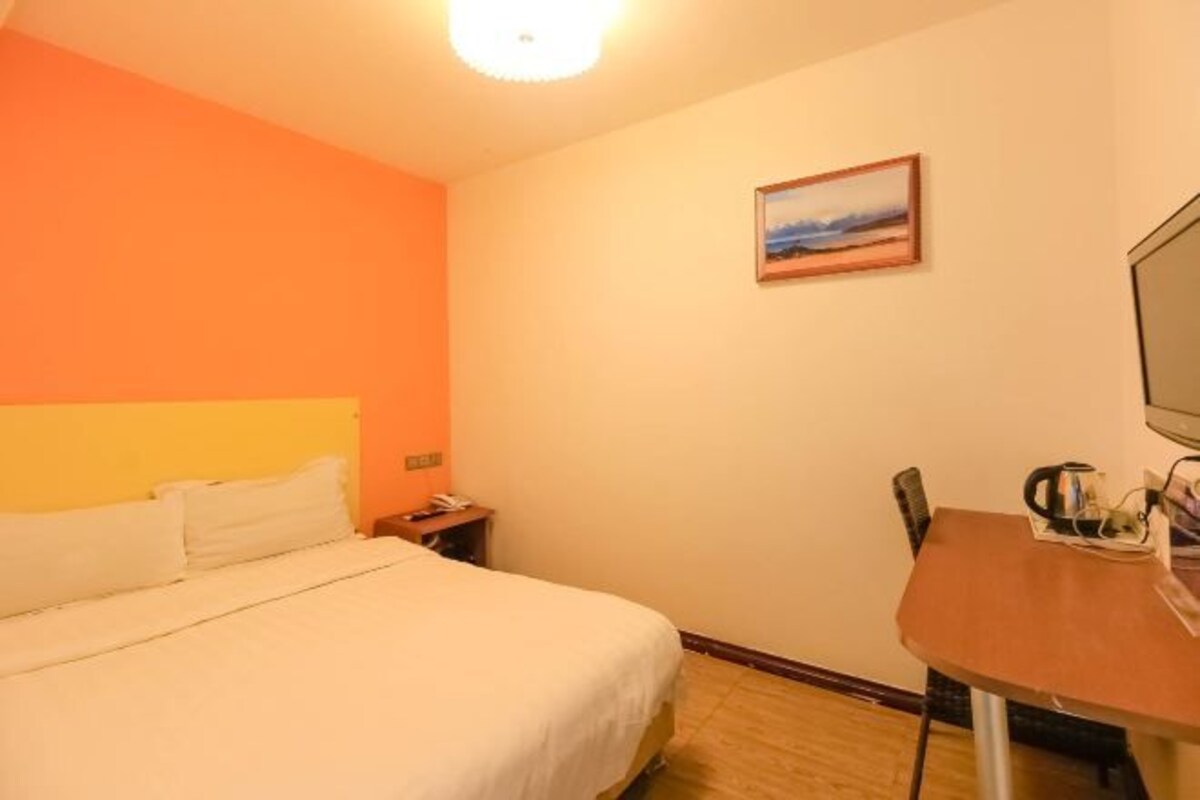 A hotel room with a bed, a desk, a chair, a television, and a painting on the wall.
