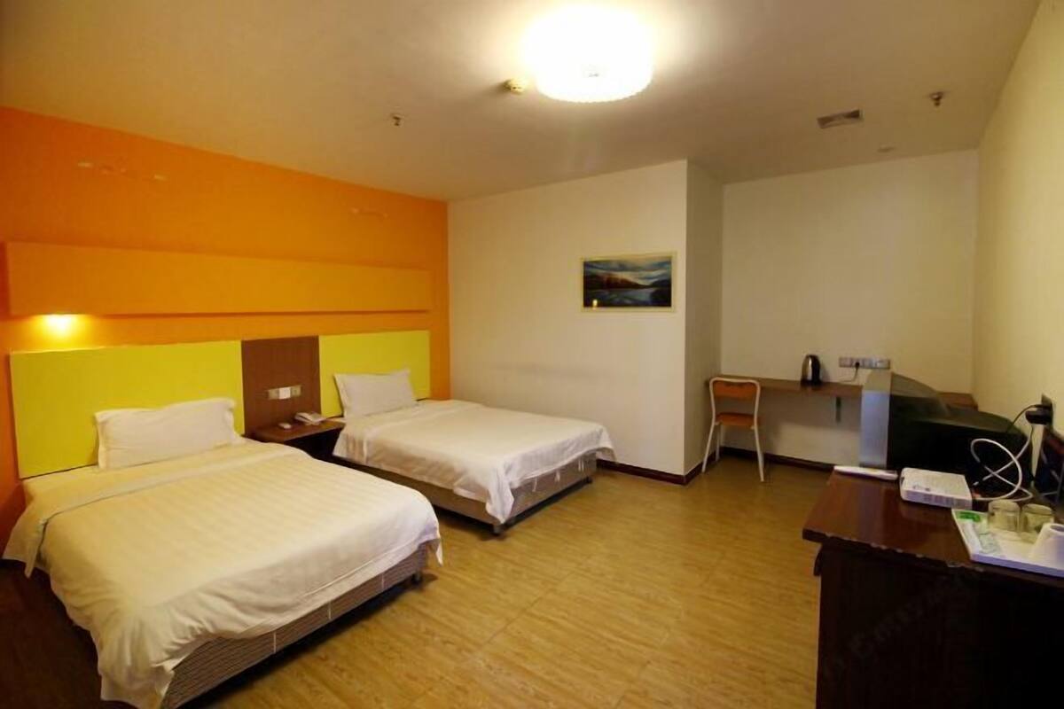 Habitación de hotel con dos camas individuales, un escritorio, una silla y una lámpara de escritorio pequeña.