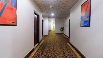 A hotel hallway with patterned carpet, framed artwork on the walls, and doors leading to rooms.
