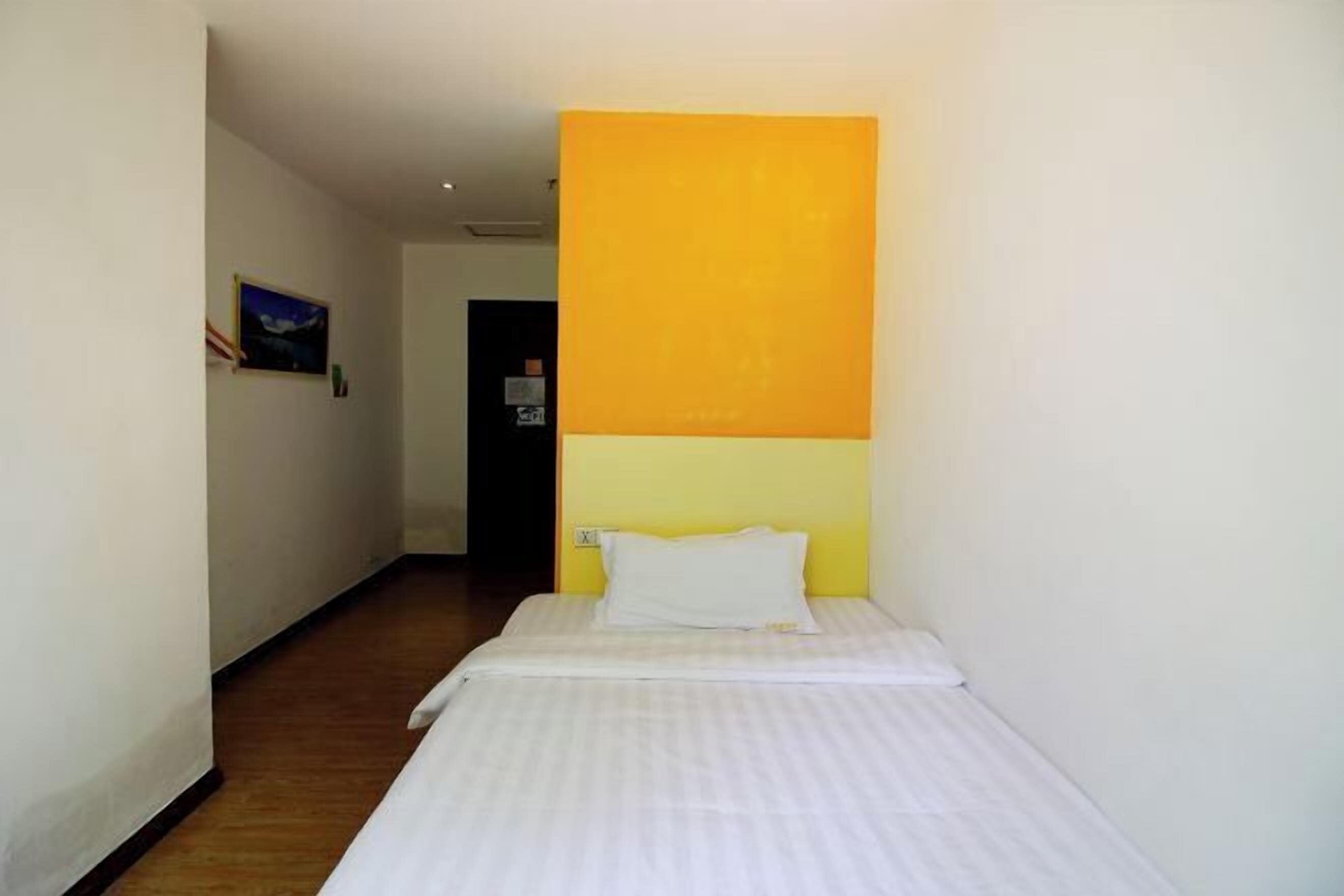 Ein Hotelzimmer mit Bett, weißem Kopfkissen und einer gelben Akzentwand.