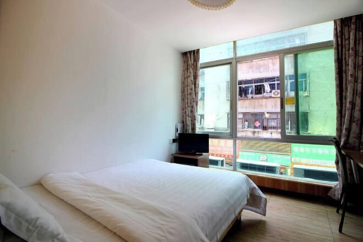 Habitación de hotel con cama, televisor sobre un mueble y ventana con vistas al exterior.