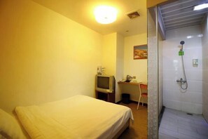 A hotel room with a bed, a desk with a computer, a television, and a shower area. - Makeboat Hotel (Zhuhai Lovers Road Riyuebei Branch) (Zhuhai)