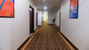 Un couloir avec un tapis à motifs, des murs blancs et des affiches encadrées.