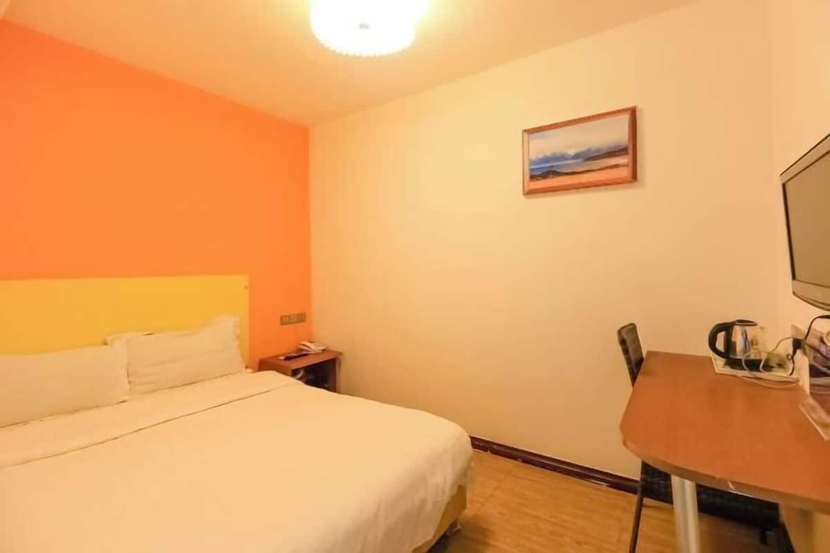 Habitación de hotel con cama, escritorio, silla, televisor y un cuadro en la pared.