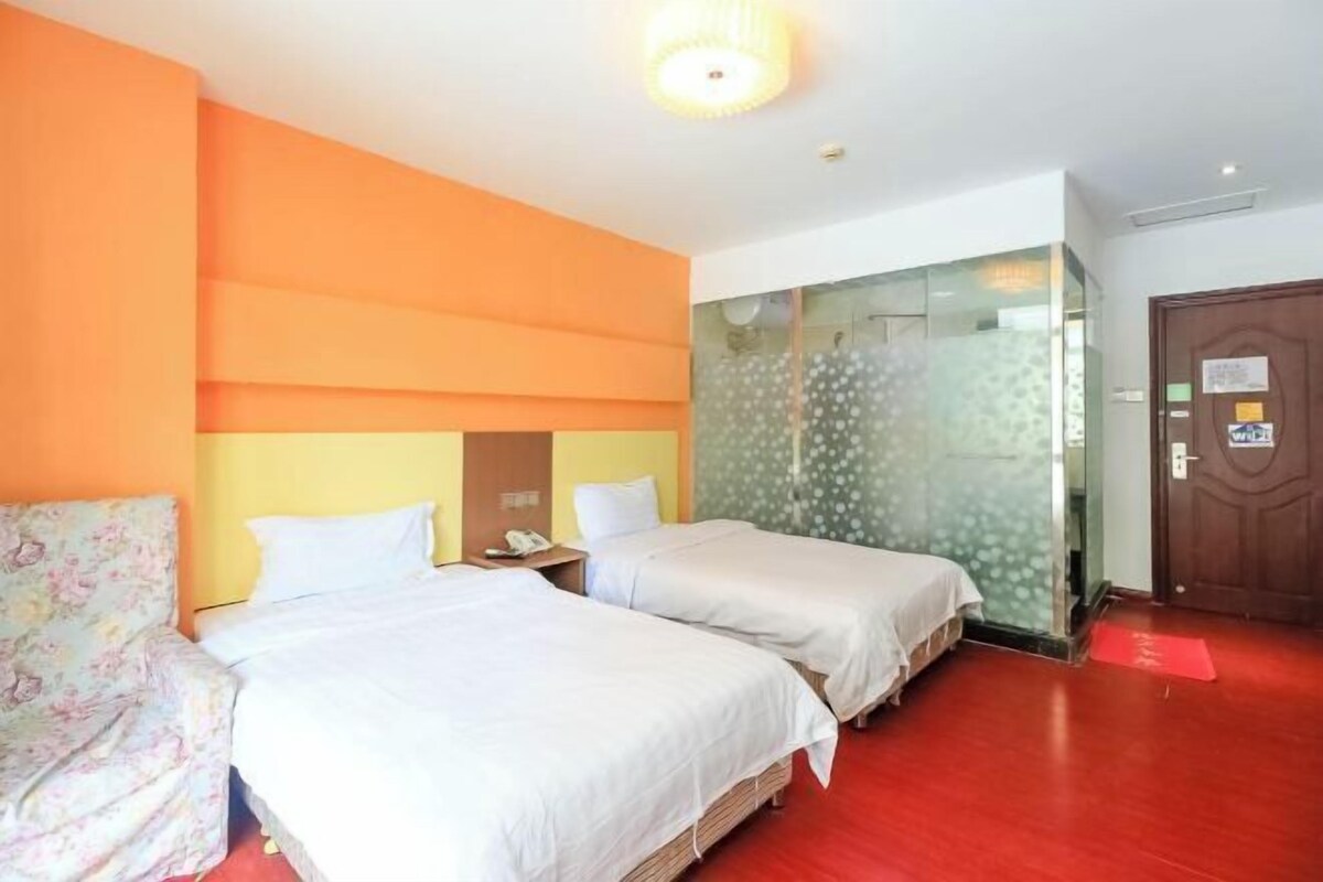 A hotel room with two beds, a wooden floor, a glass partition wall, and a wooden door.