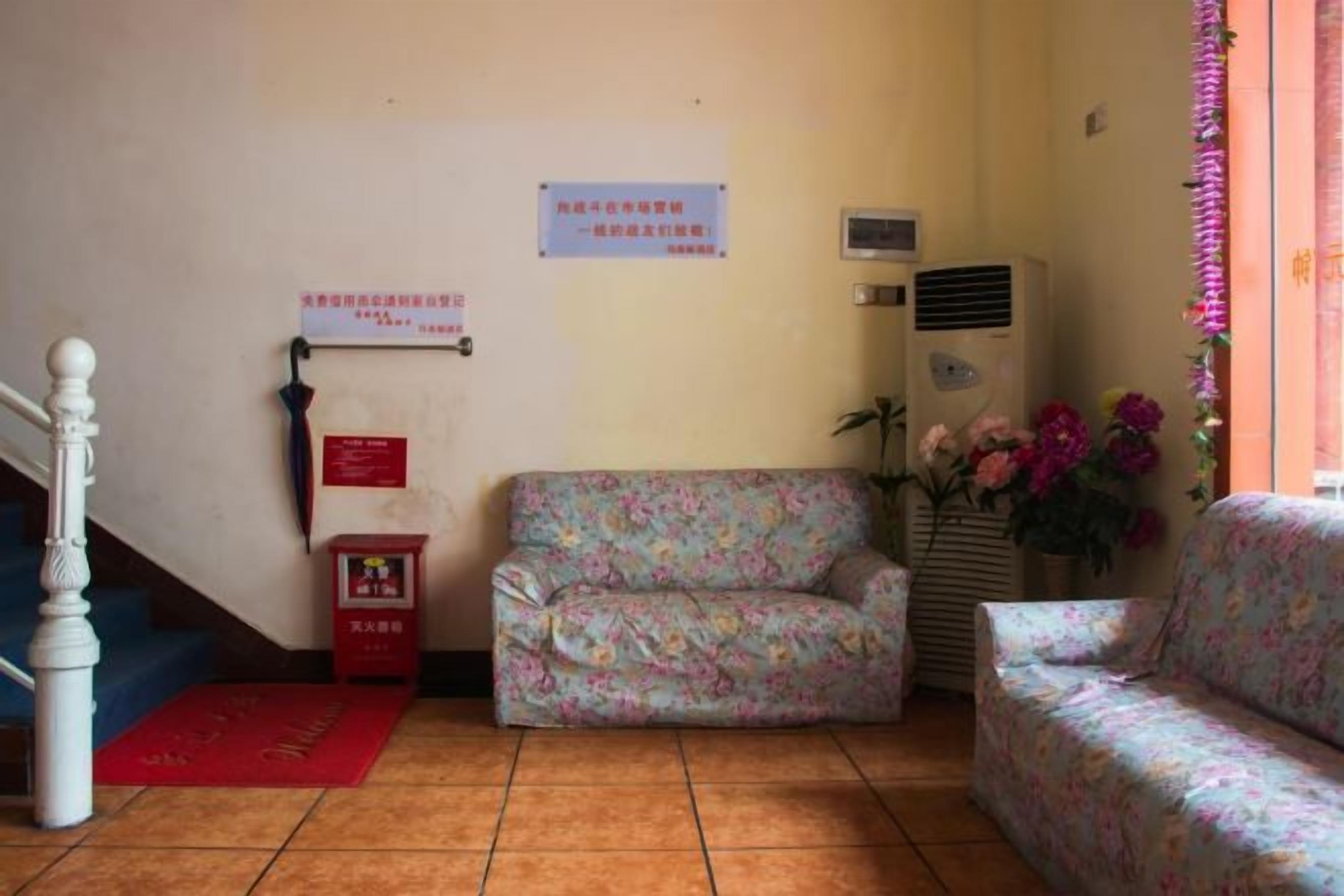 Quarto com sofá, uma mesa pequena, um armário vermelho, escada e um aviso fixado na parede.
