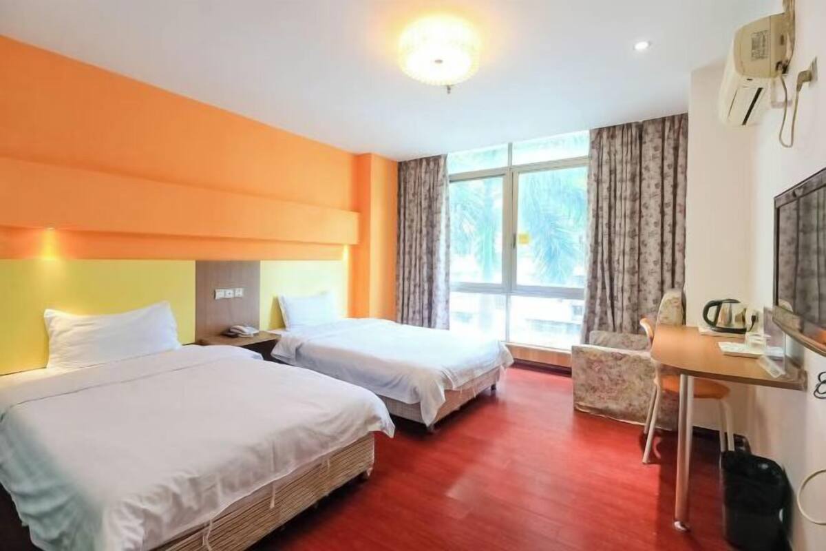 Habitación de hotel con dos camas, un escritorio, una silla y un amplio ventanal con cortinas.