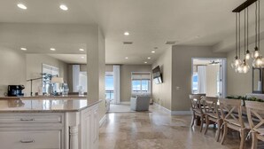 A spacious kitchen with a central island, a dining area with wooden chairs, and a view of the ocean through large windows.