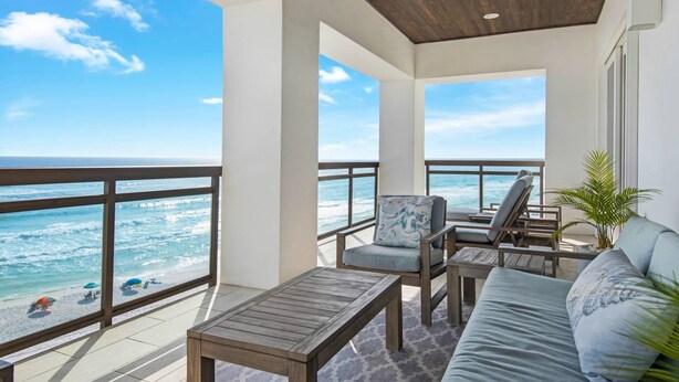 A balcony with a view of the ocean, furnished with a sofa, chairs, and a table.