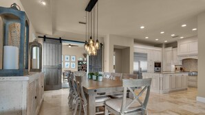 A spacious kitchen with white cabinets, a wooden dining table, and a hanging light fixture.