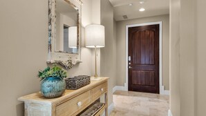 A hallway with a wooden console table, a mirror, a lamp, and a dark wooden door.