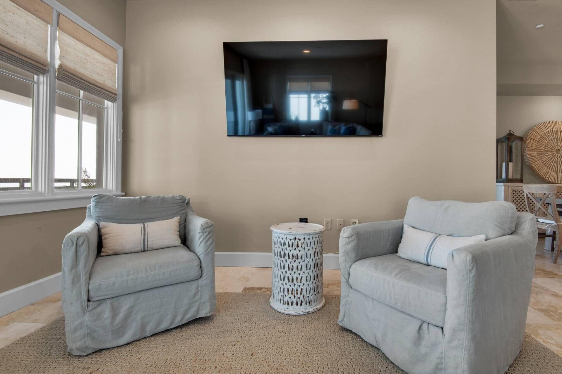 A living room with two grey armchairs, a round white side table, and a flat-screen TV mounted on the wall.