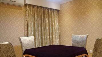 Habitación de hotel con una cama, dos sillones estampados, un ventanal con cortinas y un equipo de aire acondicionado.