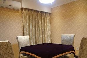 Hotellihuone, jossa on sänky, kaksi kuviollisia tuoleja, ikkuna verhoilla ja ilmastointilaite.