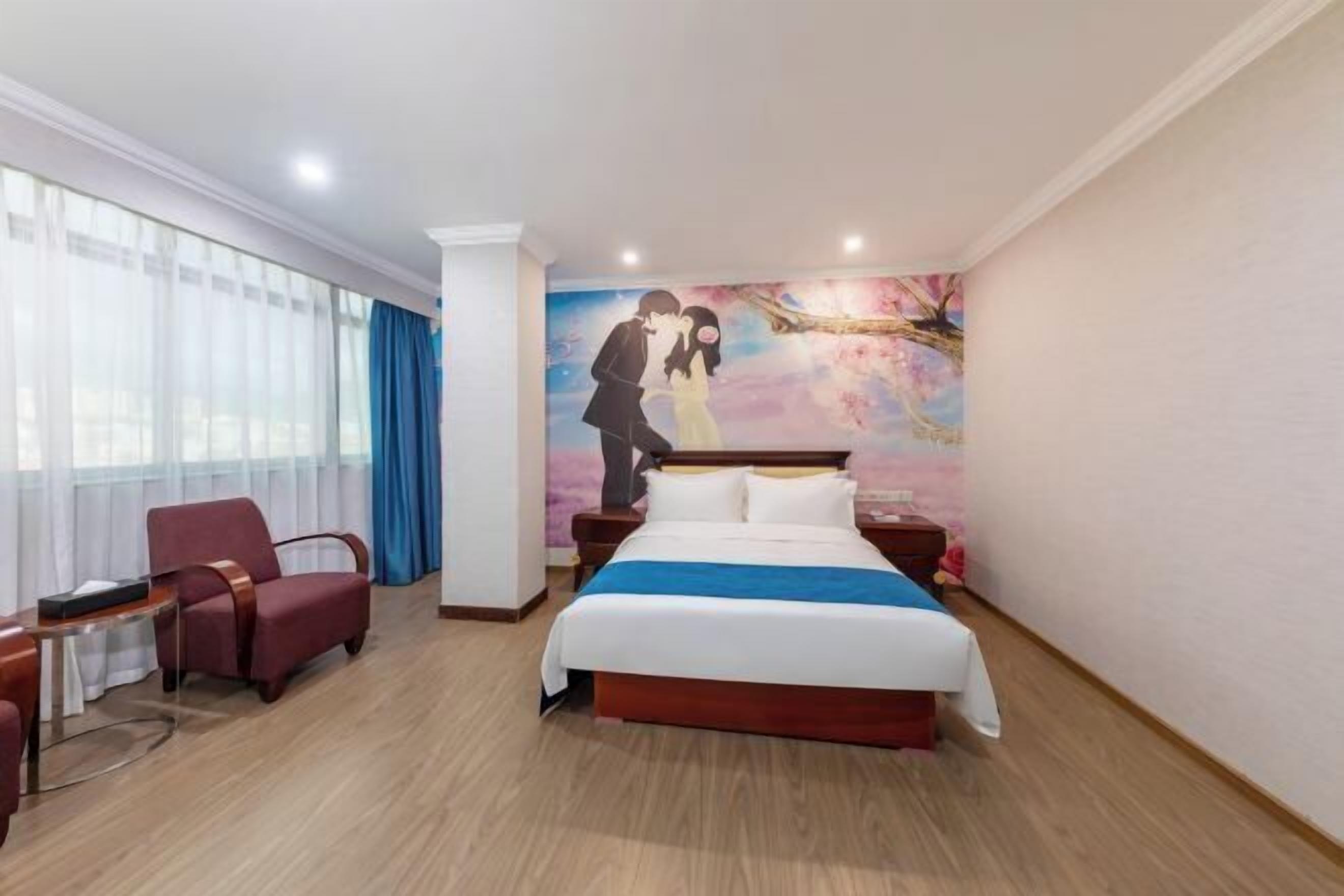A hotel room with a large bed, a chair, a small table, and a painting on the wall.