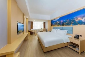 A hotel room with a large bed, a desk, a chair, a TV, and a cityscape painting on the wall. - Kuichong Holiday Hotel (Shenzhen)