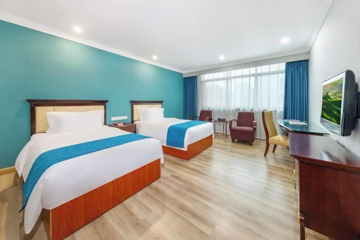 Une chambre d’hôtel avec deux lits, une télévision, un bureau et une fenêtre avec des rideaux.