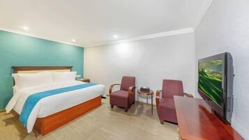 Habitación de hotel con cama, dos sillones, una mesita y televisión en la pared.