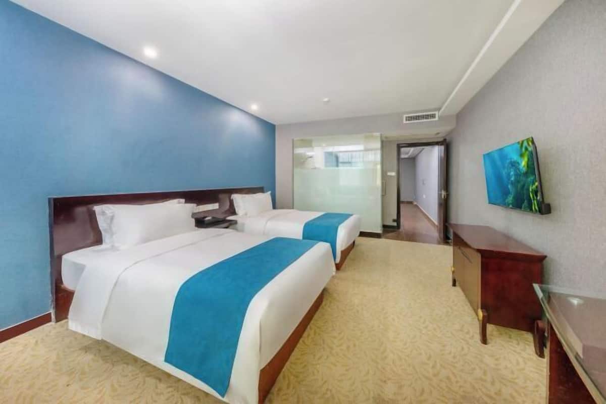 Une chambre d’hôtel avec deux lits, un bureau, une chaise et un téléviseur fixé au mur.