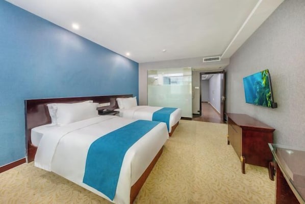 Quarto de hotel com duas camas, uma secretária, uma cadeira e uma televisão na parede.
