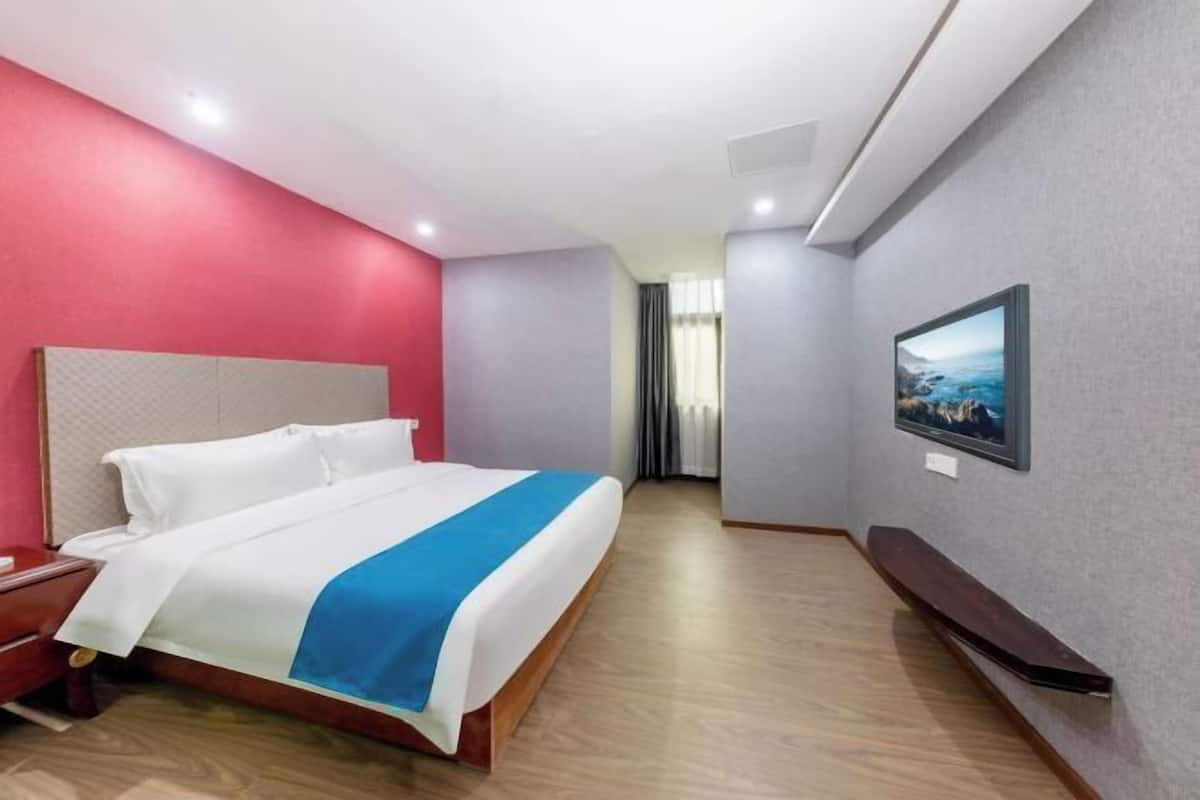 Une chambre d’hôtel avec un lit, une télévision, un plancher en bois et un mur d’accent rouge.