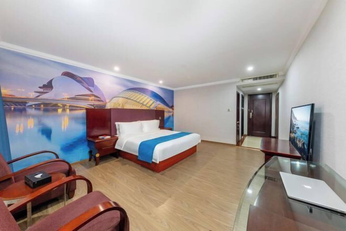 Une chambre d’hôtel avec un lit, un bureau avec un ordinateur portable, une télévision, une chaise et une fresque murale.