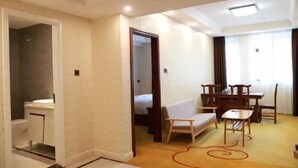 A hotel room with a bathroom, a dining area with a table and chairs, a sofa, and a carpet with a red design. - Impression Nanlin Hotel (Nanping)