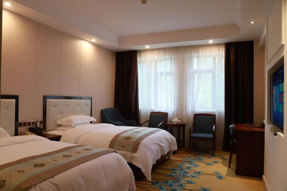 A hotel room with two beds, a desk, a chair, and a television.