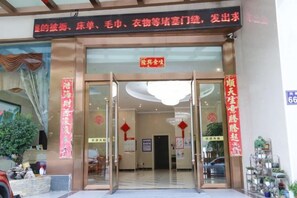 A hotel entrance with a glass door, a signboard above, and a red decoration on the wall.