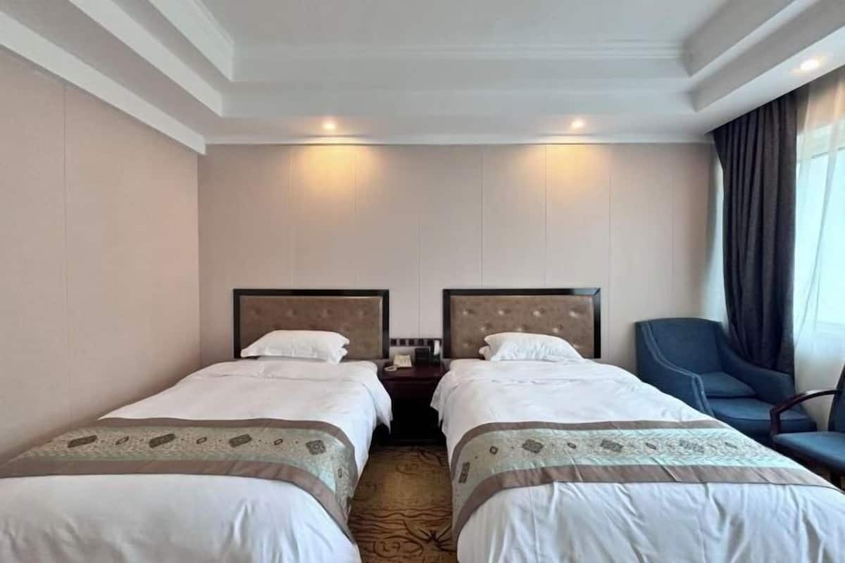 A hotel room with two beds, a nightstand, a chair, and a window with curtains.