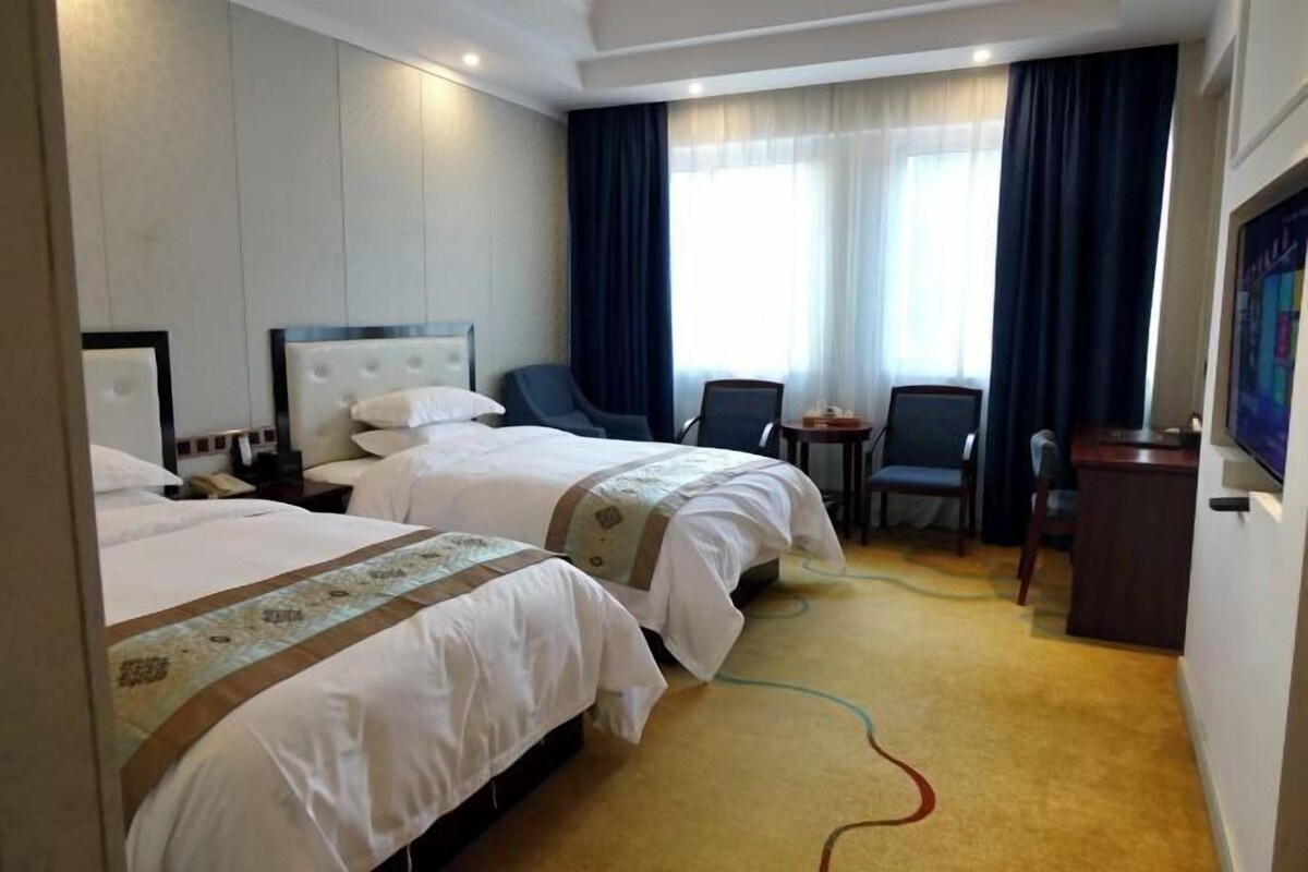 A hotel room with two beds, a desk, a chair, and a TV.