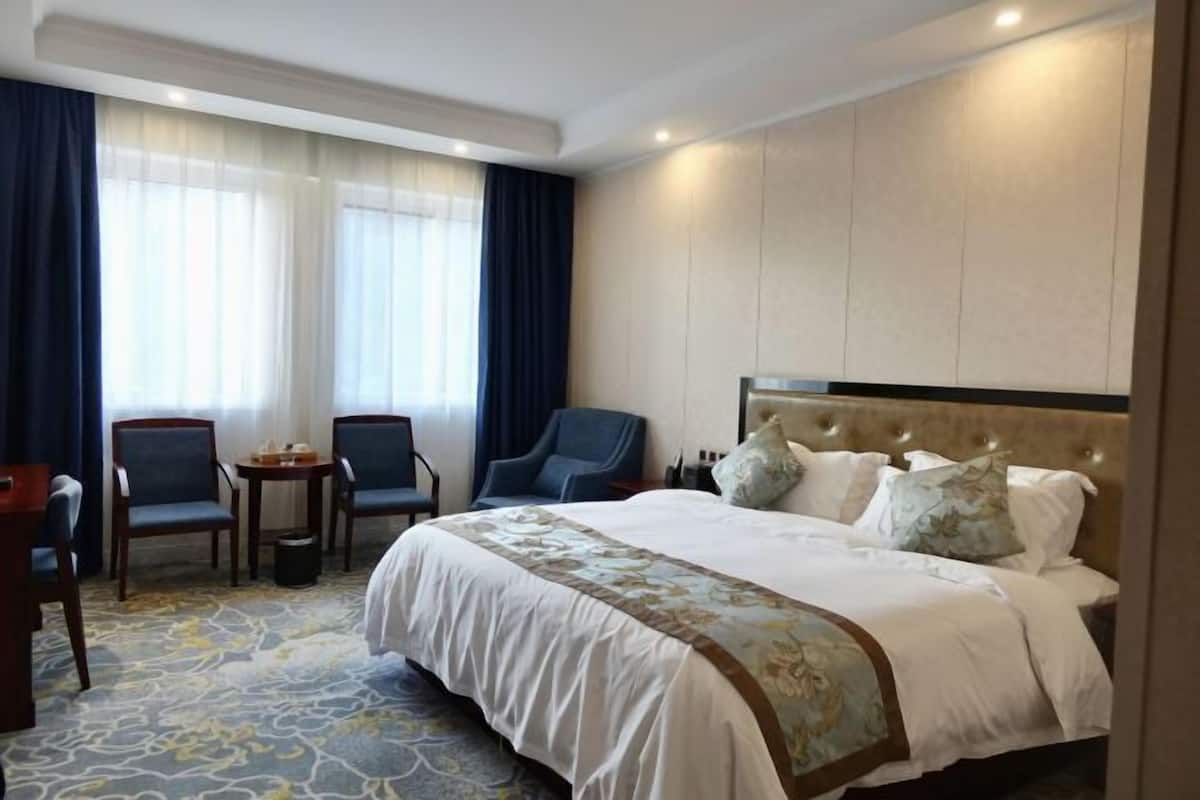 A hotel room with a large bed, two chairs, a small table, and a window with curtains.