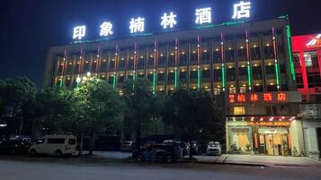 A hotel with a modern facade, illuminated signage, and a parking area in front.