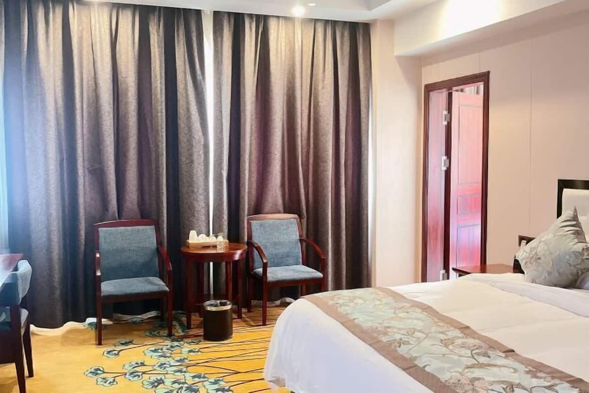 A hotel room with a bed, two armchairs, a small table, and a carpet with a floral pattern.