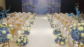 A venue with rows of chairs and floral decorations, a stage with a backdrop, and a carpeted floor.