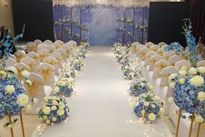A venue with rows of chairs and floral decorations, a stage with a backdrop, and a carpeted floor. - Lan Tian Business Hotel (Wuyang)